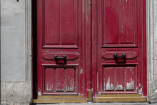 Old Wooden Door. Red Painted Wooden Double Door With Vintage Handles. Shabby Surface Of Antique Gate. Scratched Weathered Wood Textures. Architectural Details Of Paris Doorway Of Old Stone Building 