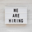'We are hiring' words on a modern board on a white wooden background, view from above. Top view, overhead, flat lay. Closeup.