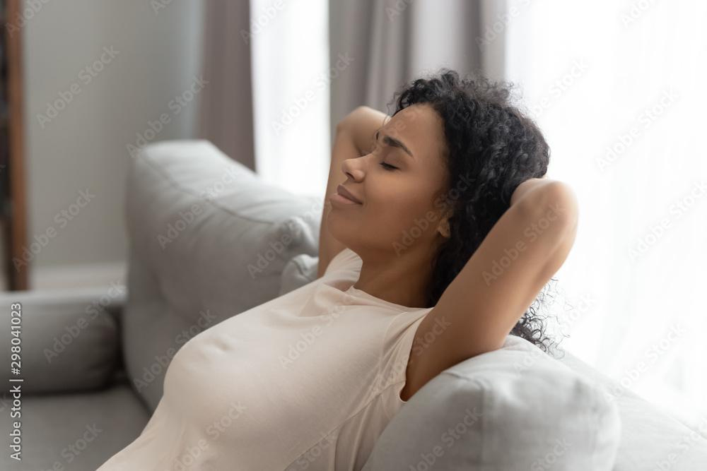 Calm black young woman relax on sofa hands over head - obrazy, fototapety, plakaty 