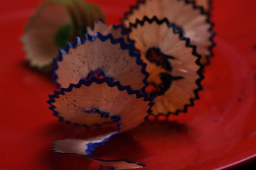 wooden shavings from colored pencils on a red background close-up