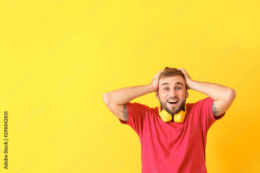 Surprised young man with headphones on color background