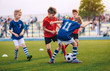 © matimix - Kids Kicking Football Ball. Boys Play Soccer on Grass Field. Spectators Parents in the Background. Youth Players kicking Soccer Match on grass Stadium. Youth Football Tournament