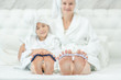 Mother and her daughter are sitting with sponge for pedicure on fingers. Mom and child girl wearing a bathrobes and with towels on their heads. Focused on the feet