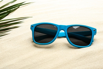 Stylish sunglasses and tropical leaf on white sand. Vacation time