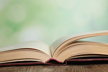 Wall Mural - Open book on wooden table against blurred green background, closeup. Space for text