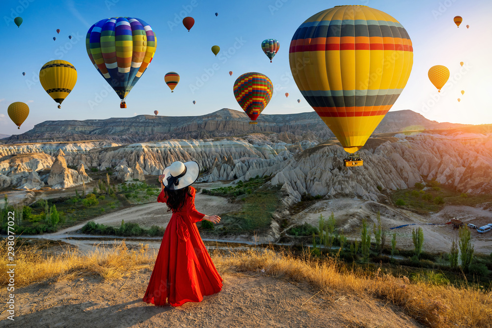 Beautiful girl standing and looking to hot air balloons in Cappadocia, Turkey. - obrazy, fototapety, plakaty 