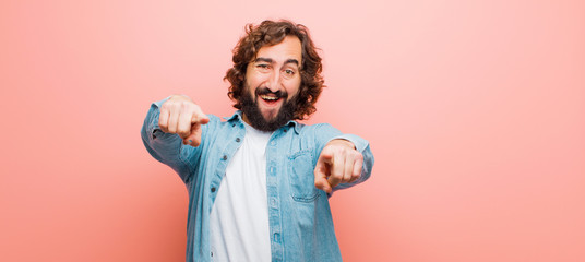 Wall Mural - young bearded crazy man feeling happy and confident, pointing to camera with both hands and laughing, choosing you against flat color wall