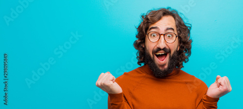 Fotomural young bearded crazy man feeling shocked, excited and happy, laughing and celebra