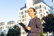 © Andres Victorero/ADDICTIVE STOCK - Serious businesswoman in elegant jacket browsing tablet and looking away while standing on city street on sunny day