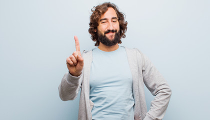 young bearded crazy man smiling and looking friendly, showing number one or first with hand forward,