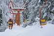Chair ski lift next to slope for skis and snowboards. Skiers are sitting at old fashioned chair ski lift. Ski area in snowy high mountain. Sports and recreation concept. Selective focus.