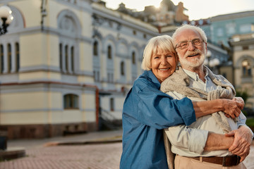 True love has no expiration date. Portrait of cheerful senior couple in casual clothing embracing each other and looking at camera with smile while standing together outdoors