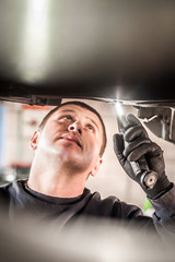 Wall Mural - Auto mechanic repairer checking condition under car on vehicle lift