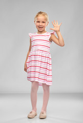 Wall Mural - childhood and people concept - smiling little girl in striped dress waving hand over grey background