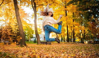 Happy young woman jumping with raised arms on colorful autumn leaves city background