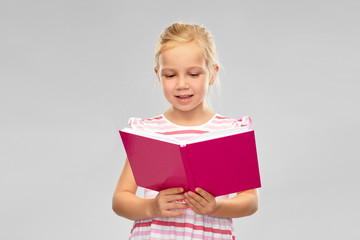 Wall Mural - childhood and people concept - smiling little girl reading book over grey background