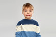 childhood, expressions and people concept - shocked little boy in striped pullover over grey background