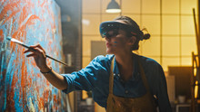 Talented Female Artist Wearing Augmented Reality Headset Working On Abstract Painting, Uses Paint Brush To Create New Concept Art Using Virtual Reality Interface. High Tech Creative Modern Studio