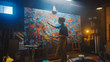 © Gorodenkoff - Talented Female Artist Working on a Modern Abstract Oil Painting, Gesturing with Broad Strokes Using Paint Brush. Dark Creative Studio Large Picture Stands on Easel Illuminated, Tools Everywhere