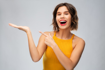 Sticker - emotions and people concept - happy smiling young woman in mustard yellow top holding something on empty hand over grey background