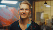 © Gorodenkoff - Talented Young Artist Dirty with Paint, Wearing Stylish Glasses Looks at the Camera he Smiles. Messy Creative Studio with Large Canvas