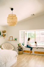 Mom And Child Sitting In Bay Window In Bedroom