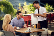 © Drazen - Young smiling waiter setting table for dining to his guests in a restaurant.