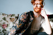 © Thais Ramos Varela/Stocksy - Portrait of young redhead man sitting on sofa
