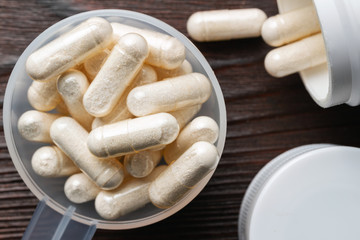 White medical capsules of glucosamine chondroitin, healthy supplement pills in the plastic spoon on wooden background, macro image, top view