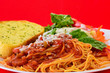 Closeup of Spaghetti with Garlic Bread and Salad on Red Background with Copy Space