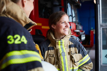Smiling Female Firefighter Standing With Coworker In Fire Station