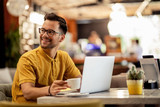 Fototapeta Londyn - Smiling man enjoying in coffee break while using laptop in a cafe.