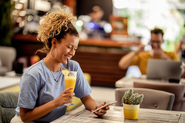 Happy woman drinking juice and using smart phone in a cafe.