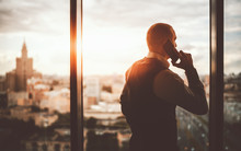 Silhouette Of A Prosperous Man Entrepreneur Standing Near The Panoramic Window Of A Luxurious Business Office Skyscraper And Pensively Looking On An Evening Cityscape While Talking On The Phone