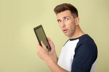 Sticker - Shocked young man with tablet computer on color background