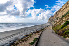 An Asphalt Path Leading To The Sandy Shores Of La Jolla, San Diego, California, With A Serene View Of The Pacific Ocean And Sandstone Cliffs Towering Over The Flat Black Sandy Beach.