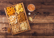 Glass of craft lager beer and opener with box of snacks on wooden background. Pretzel,salty potato sticks, peanuts, onion rings with nachos in vintage box with openers and beer mats. Space for text
