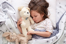 Close Up Portrait Of Beautiful Cute Little Girl Sleeping Peacefully And Hugging Her Stuffed Toys In Bed, Charming Kid With Closed Eyes, Dark Haired Child Relaxing At Home In Morning. Childhood Concept