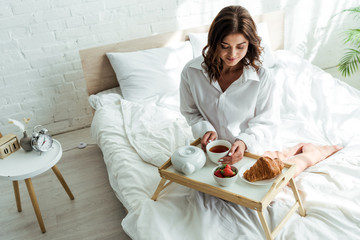 attractive woman in white shirt having breakfast in bed at morning