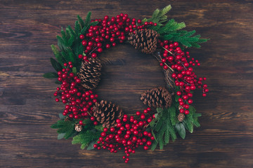 Wall Mural - Top above high angle view photo of winter christmas traditional seasonal wreath with green fir tree leaves pine cone red mistletoe berries lay on brown wooden table isolated
