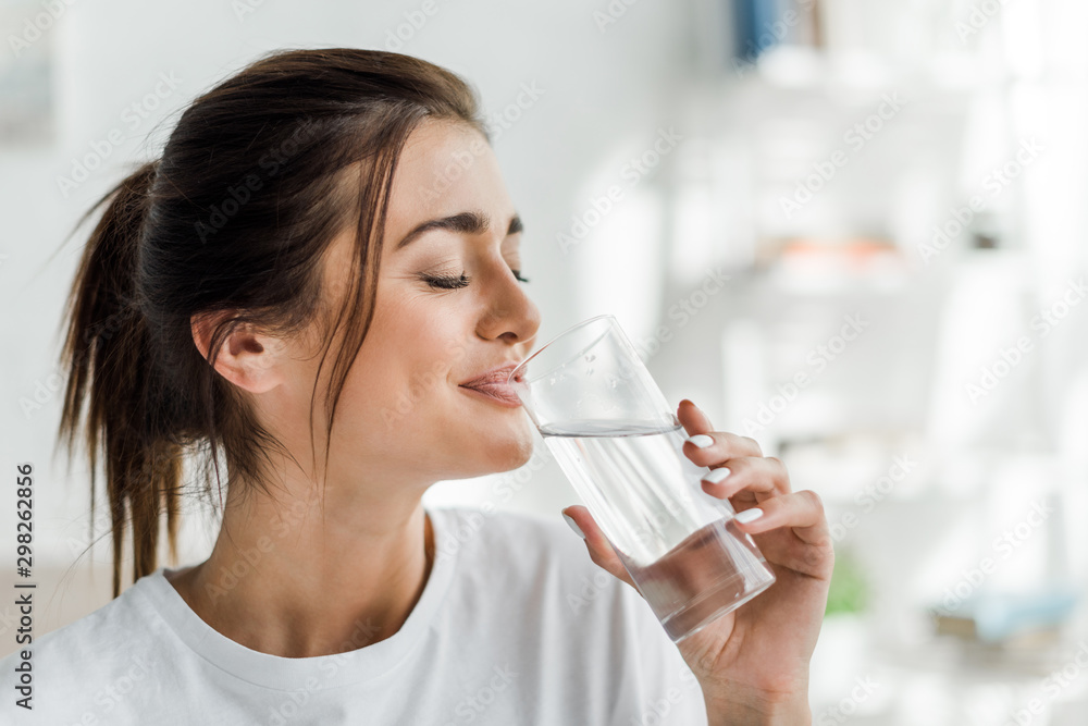 smiling girl holding drinking water from glass in the morning - obrazy, fototapety, plakaty 
