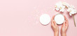 Young woman holding a opened container with cosmetic cream lotion body milk White Phalaenopsis orchid flowers festive confetti on pink background Flat lay top view minimalism style Beauty concept