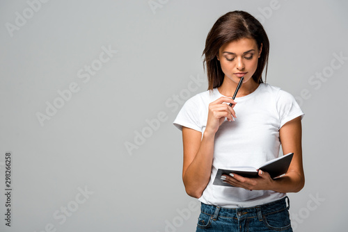Cuadros en Lienzo pensive young woman holding pen and notebook, isolated on grey
