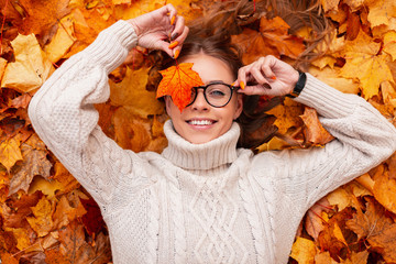 funny young hipster woman with a positive smile with an orange maple leaf in glasses in a trendy kni