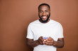 © deagreez - Photo of cheerful positive handsome man holding telephone searching for new information smiling toothily isolated over brown pastel color background