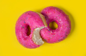 Two sweet pink donuts isolated on yellow background. A half-eaten bagel. Bright tasty bun. Minimal summer concept. Flat lay. The concept of unhealthy eating and weight gain. Harmful fast food