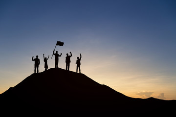 Wall Mural - Silhouette of people are celebrating success at the top of the mountain, sky and sun light background. Team business concept.