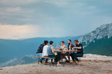 Wall Mural - Friends and family gathered for picnic dinner for Thanksgiving. Festive young people celebrating life with red wine, grapes, cheese platter, and a selection of cold meats