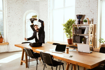 Wall Mural - Young caucasian businessman having fun dancing break dance in the modern office at work time with gadgets. Management, freedom, professional occupation, alternative way of working. Loves his job.