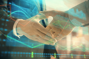 Double exposure of financial graph on cityscape background with two businessman handshake. Concept of stock market deal